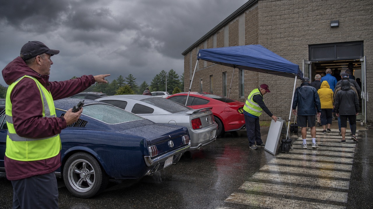 Mustang club volunteers guide entrants into a solid building as rain reaches the show field